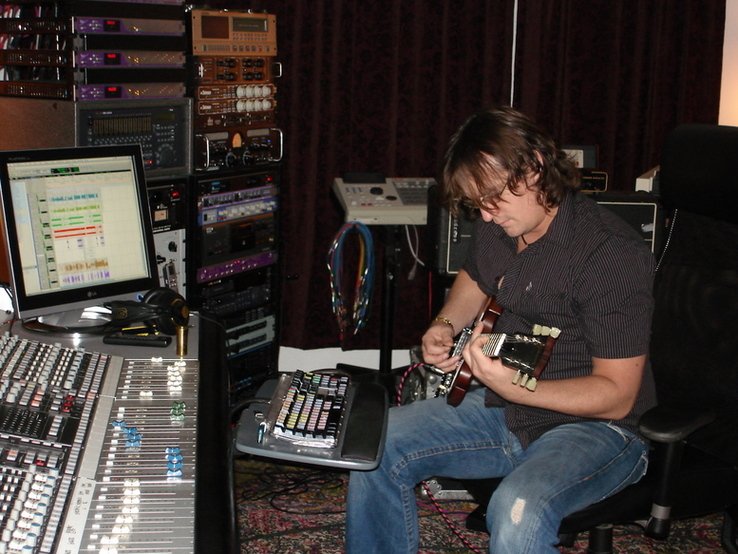 Randy Lane playing guitar at the mixing console in his studio, writing a song